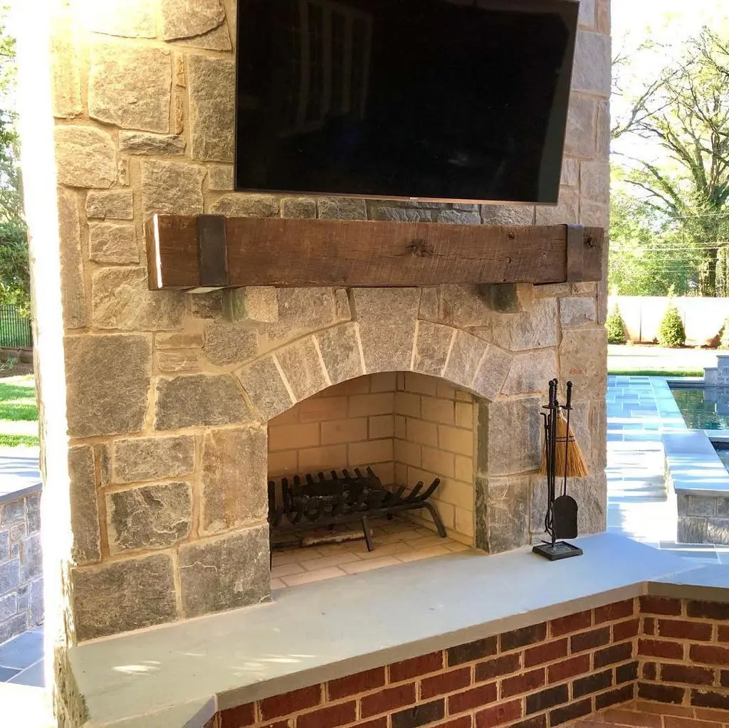 An outdoor fireplace with a tv mounted above it in a mountain home.