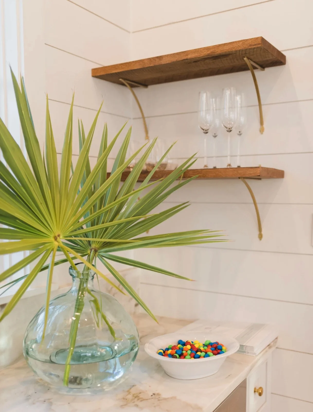 Wooden shelves with glasses on them and a plant in front.